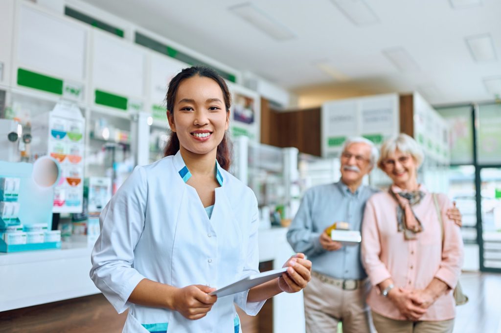 Happy Chinese pharmacist at work with her customers in the background.